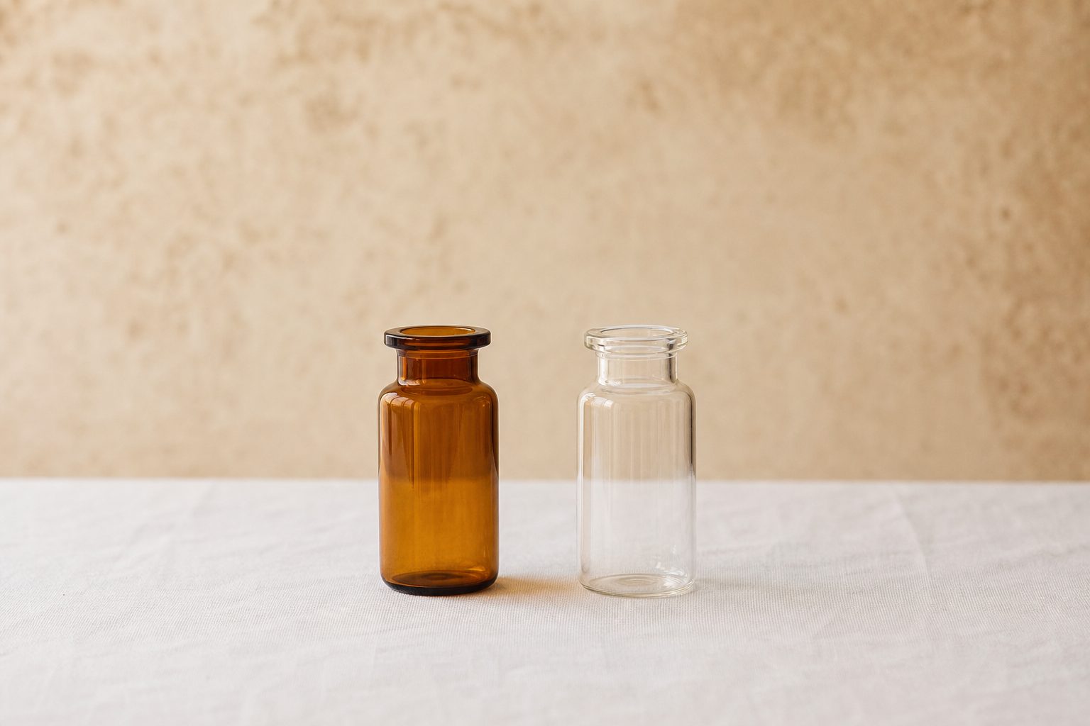 Two small glass hormone vials side by side on a bright linen white surface